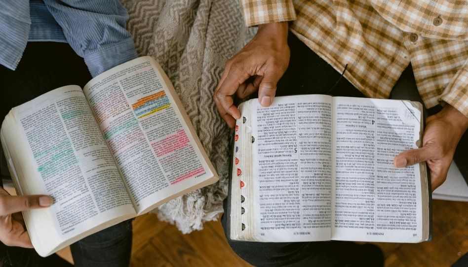 Duas pessoas sentadas juntas estudando o Velho Testamento na Bíblia, para ter experiências.